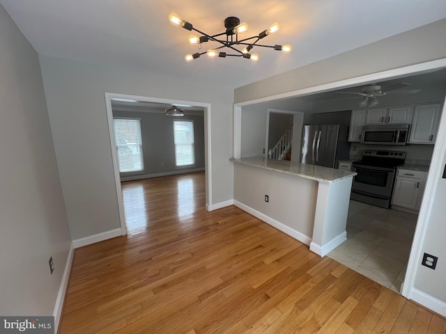 kitchen with light hardwood / wood-style flooring, appliances with stainless steel finishes, kitchen peninsula, light stone countertops, and ceiling fan with notable chandelier