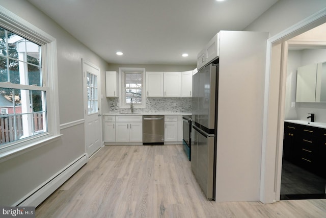 kitchen featuring sink, white cabinetry, a baseboard heating unit, stainless steel appliances, and light hardwood / wood-style floors