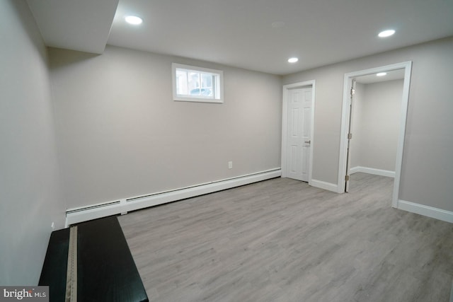 basement featuring a baseboard heating unit and light hardwood / wood-style floors