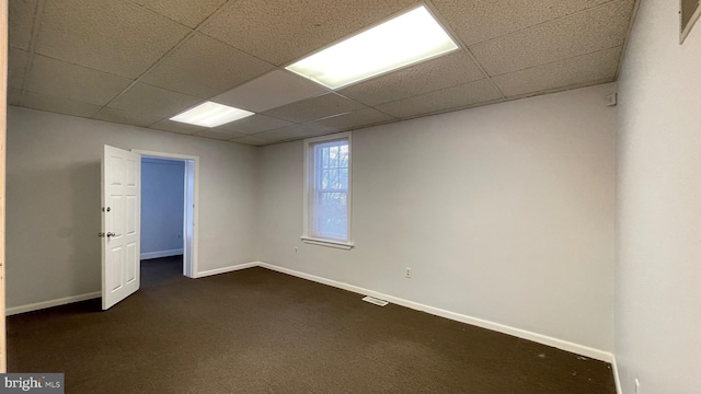 spare room featuring a paneled ceiling and dark colored carpet