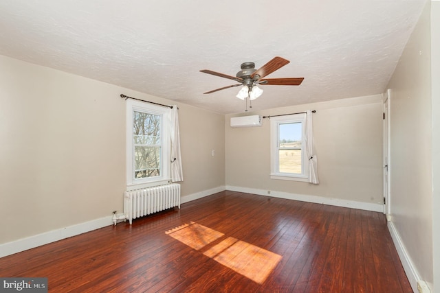 spare room with a healthy amount of sunlight, dark hardwood / wood-style flooring, radiator, and an AC wall unit