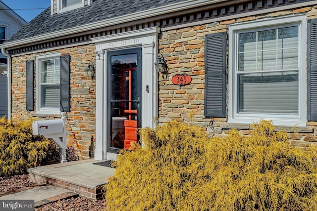 view of exterior entry featuring a shingled roof and stone siding