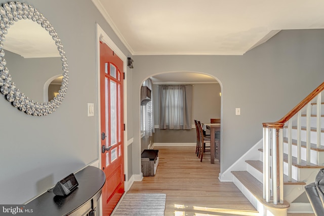 foyer entrance with arched walkways, ornamental molding, stairs, and light wood-style floors