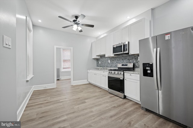 kitchen featuring light stone countertops, appliances with stainless steel finishes, white cabinets, and backsplash