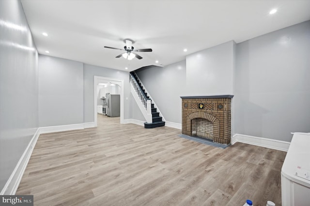 unfurnished living room with a brick fireplace, ceiling fan, and light wood-type flooring