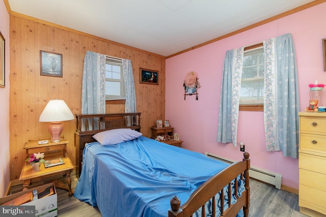 bedroom featuring a baseboard heating unit, wood-type flooring, ornamental molding, and wood walls