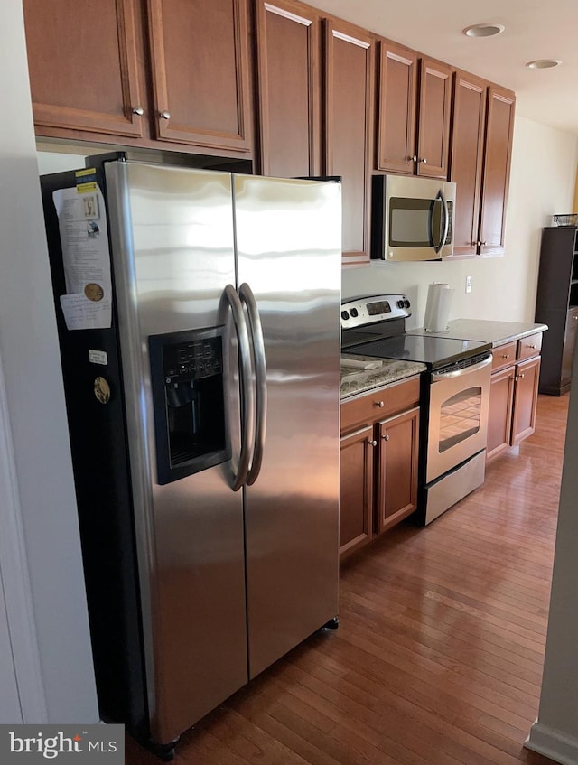 kitchen featuring wood-type flooring, appliances with stainless steel finishes, and dark stone counters