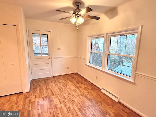 interior space with a baseboard heating unit, ceiling fan, light wood-type flooring, and plenty of natural light