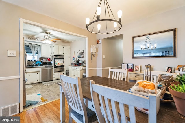 dining space with ceiling fan with notable chandelier and light hardwood / wood-style floors