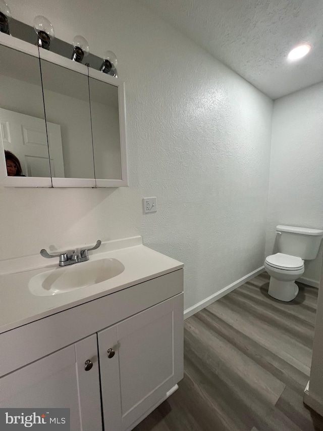 bathroom with wood-type flooring, toilet, vanity, and a textured ceiling