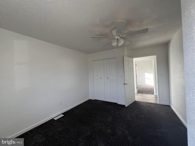 unfurnished bedroom with ceiling fan, dark carpet, a closet, and a textured ceiling