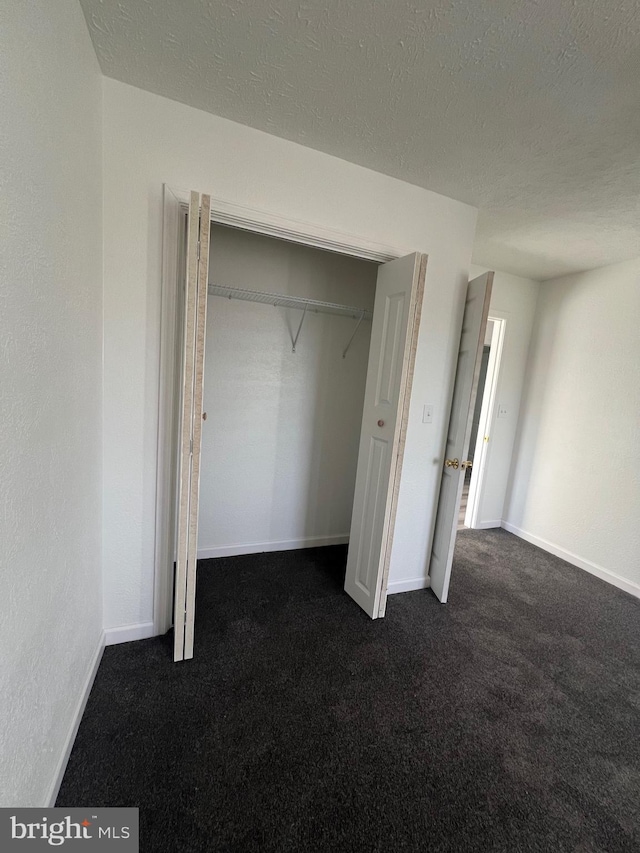 unfurnished bedroom with dark carpet, a closet, and a textured ceiling