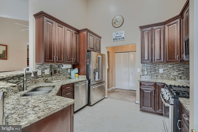 kitchen featuring appliances with stainless steel finishes, sink, decorative backsplash, a high ceiling, and light stone counters