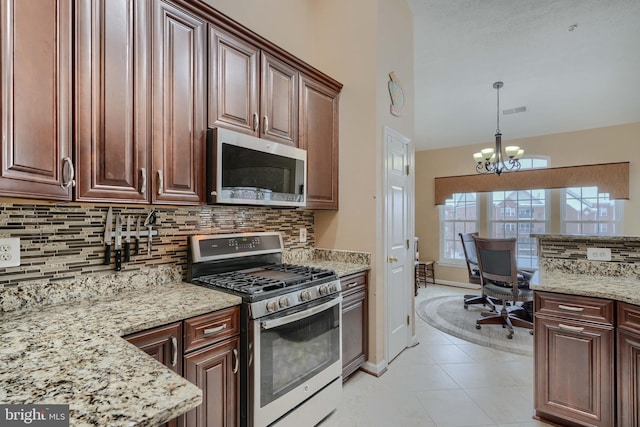 kitchen with light tile patterned floors, appliances with stainless steel finishes, hanging light fixtures, light stone counters, and decorative backsplash