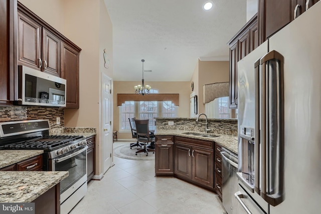 kitchen featuring decorative light fixtures, sink, backsplash, light stone counters, and stainless steel appliances