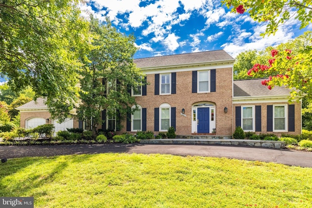 colonial home with brick siding, a shingled roof, and a front lawn