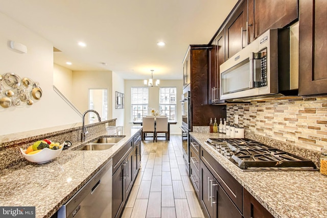 kitchen with sink, decorative backsplash, hanging light fixtures, stainless steel appliances, and light stone countertops