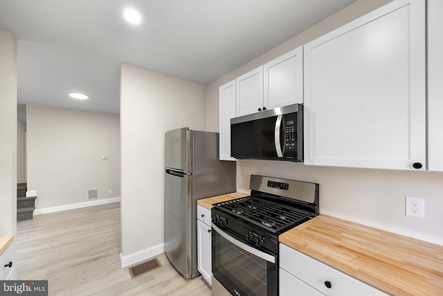 kitchen featuring appliances with stainless steel finishes, butcher block countertops, light wood-type flooring, and white cabinets