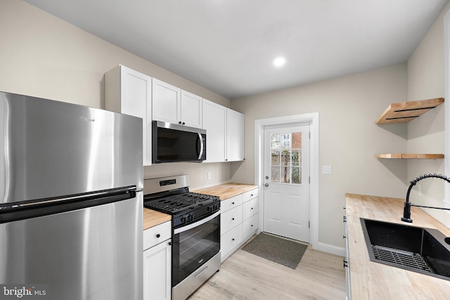 kitchen with butcher block countertops, sink, white cabinets, stainless steel appliances, and light wood-type flooring