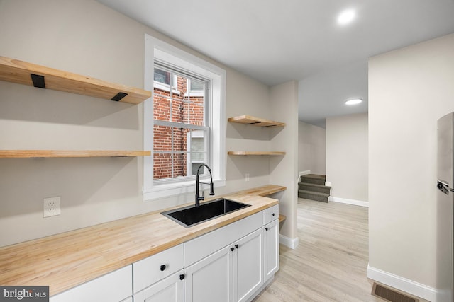 kitchen featuring wood counters, sink, white cabinetry, and light hardwood / wood-style flooring