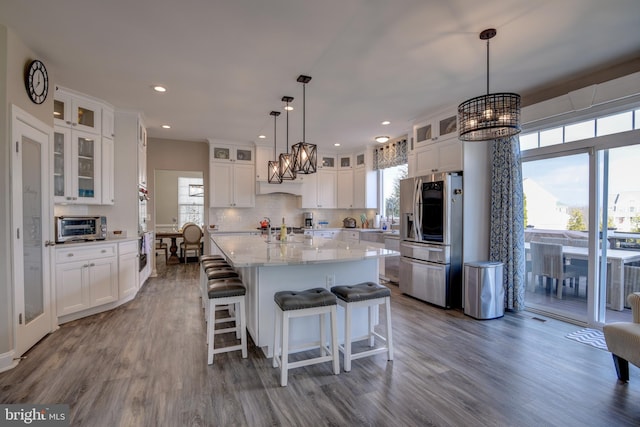 kitchen with stainless steel refrigerator, hanging light fixtures, backsplash, an island with sink, and white cabinets