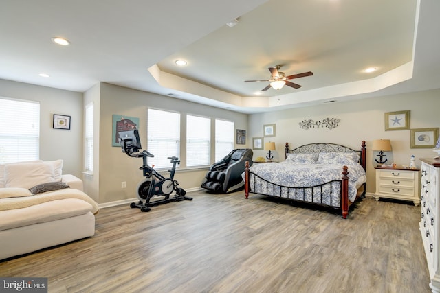 bedroom with hardwood / wood-style floors, ceiling fan, and a tray ceiling