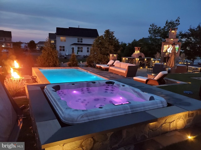 pool at dusk with an outdoor hot tub and an outdoor living space