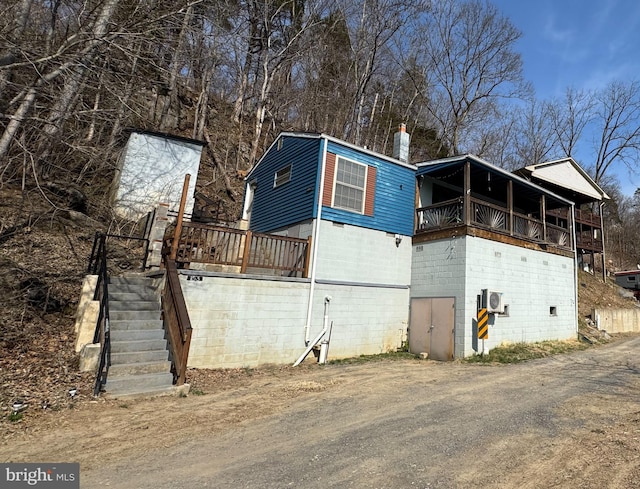 view of side of property featuring a chimney, concrete block siding, and stairs