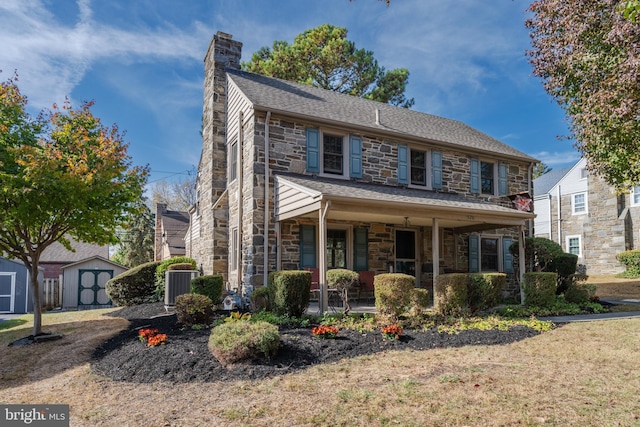 colonial house featuring a porch, cooling unit, and a storage shed