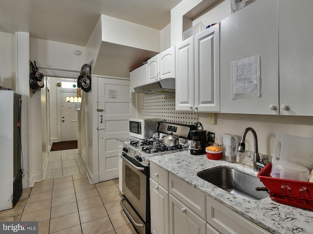 kitchen featuring sink, light tile patterned floors, stainless steel gas range, refrigerator, and white cabinets