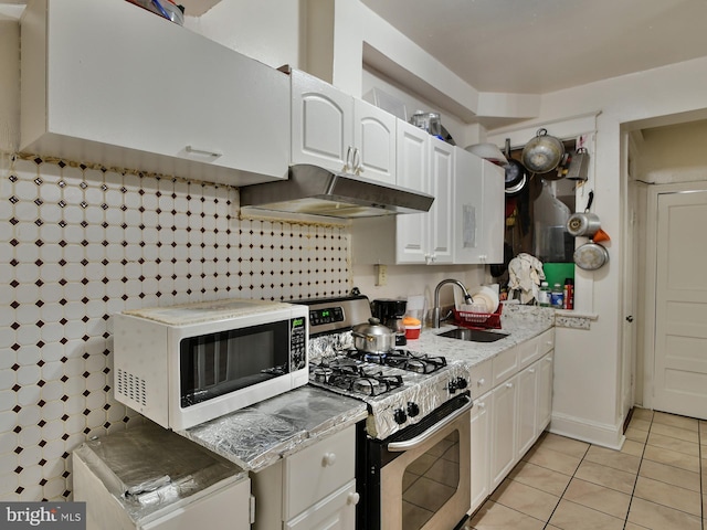 kitchen featuring gas range, white cabinetry, light tile patterned flooring, and sink