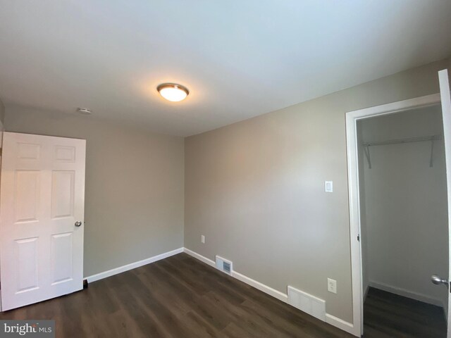 unfurnished bedroom with a walk in closet, dark hardwood / wood-style flooring, and a closet