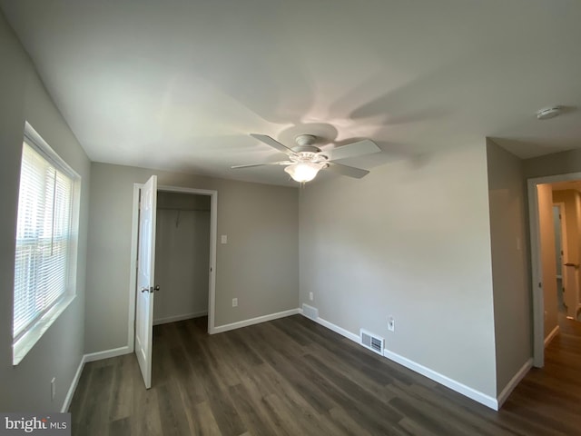 unfurnished bedroom with ceiling fan, dark hardwood / wood-style flooring, a closet, and a walk in closet