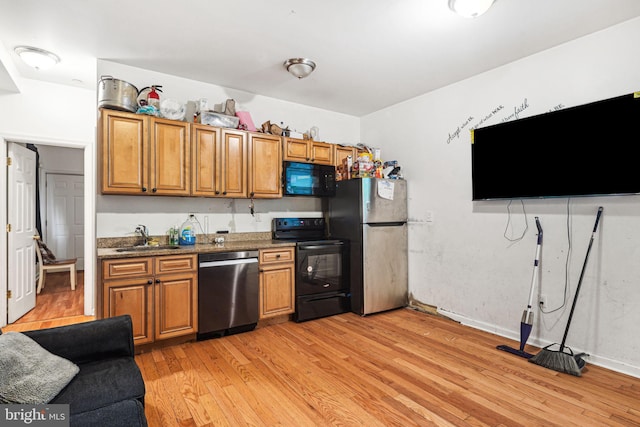 kitchen with dark stone counters, light hardwood / wood-style floors, sink, and black appliances