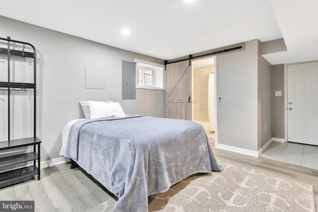 bedroom with a barn door, electric panel, and light hardwood / wood-style floors