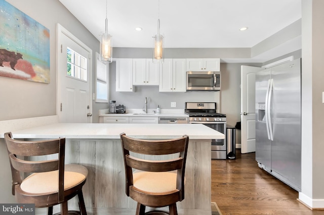 kitchen featuring appliances with stainless steel finishes, white cabinets, dark hardwood / wood-style flooring, decorative light fixtures, and kitchen peninsula