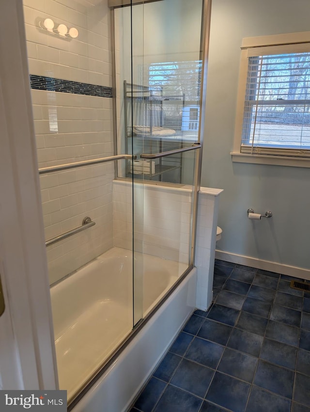 bathroom featuring toilet, bath / shower combo with glass door, and tile patterned flooring