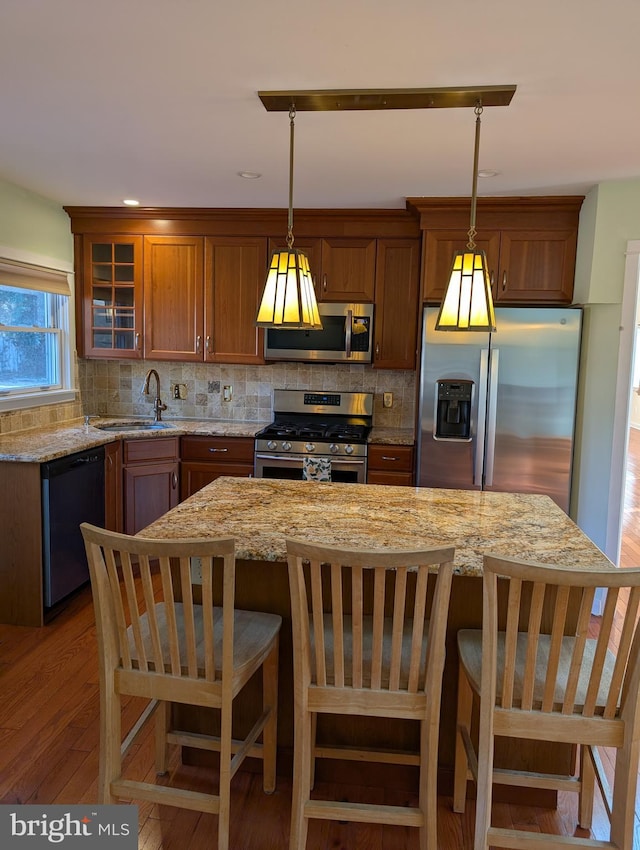 kitchen with tasteful backsplash, light stone counters, appliances with stainless steel finishes, a kitchen breakfast bar, and pendant lighting