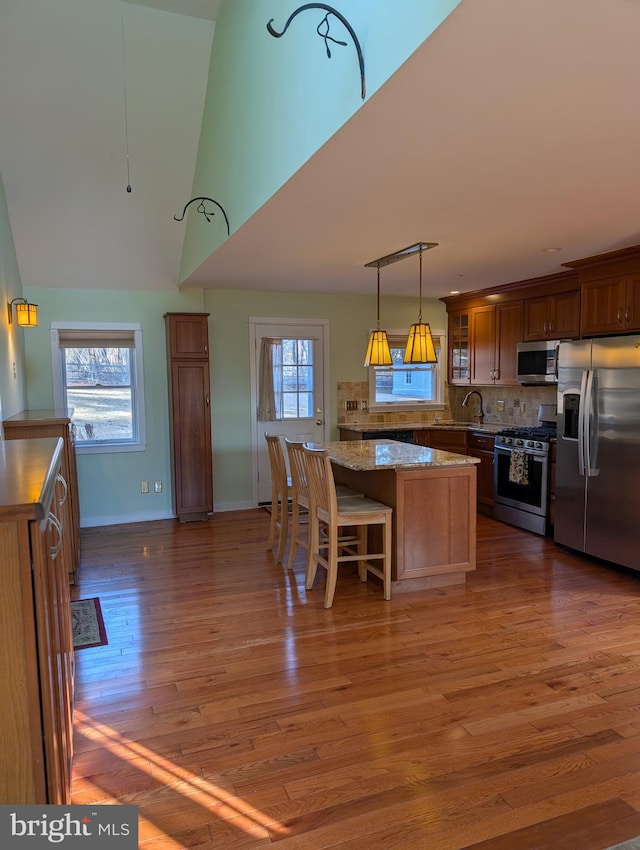 kitchen with dark hardwood / wood-style floors, hanging light fixtures, a center island, stainless steel appliances, and light stone countertops