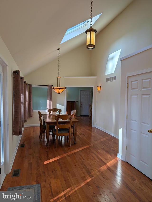 dining area with dark hardwood / wood-style floors, high vaulted ceiling, and a skylight