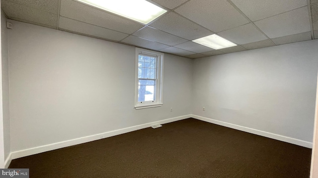 unfurnished room with dark colored carpet and a drop ceiling