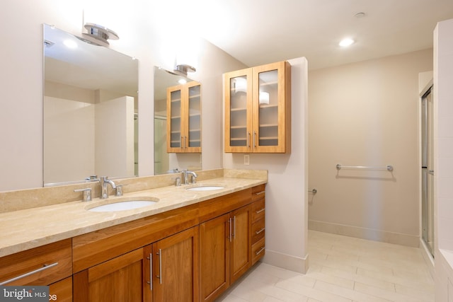 bathroom featuring double vanity, baseboards, a sink, and a shower with shower door