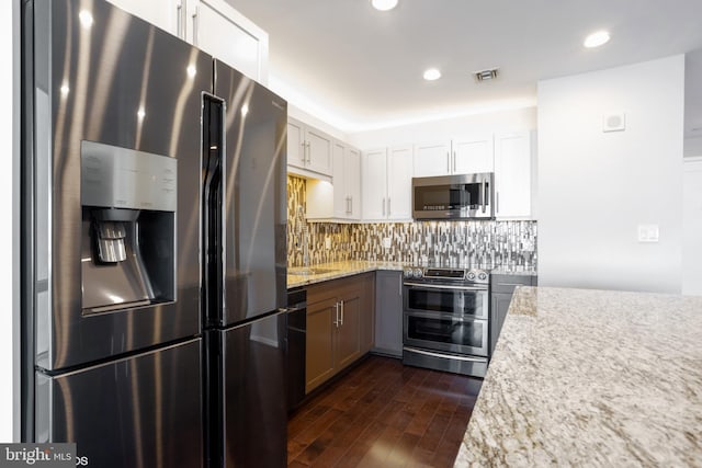 kitchen with light stone counters, dark wood-style flooring, white cabinets, appliances with stainless steel finishes, and backsplash