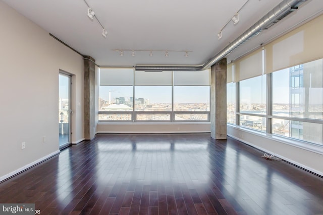 unfurnished room with dark wood-type flooring, rail lighting, and a city view