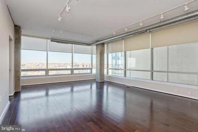 empty room featuring dark wood-type flooring, a city view, and track lighting