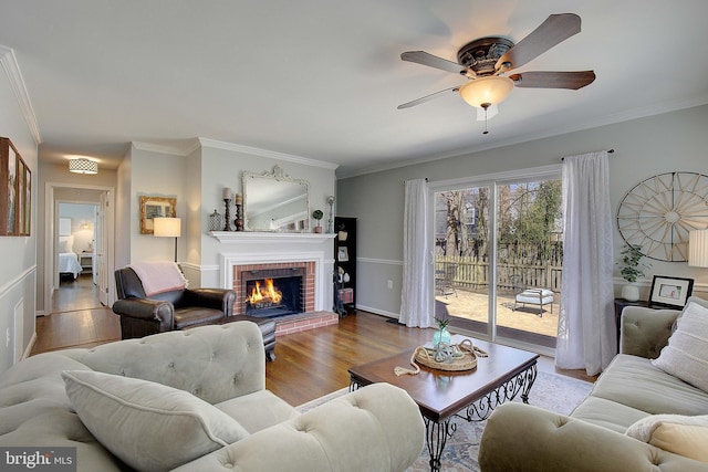 living area featuring a brick fireplace, baseboards, ornamental molding, wood finished floors, and a ceiling fan