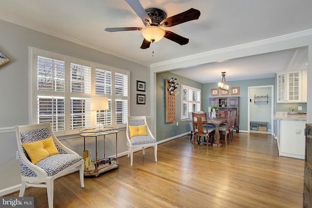 living area featuring baseboards, light wood-style floors, crown molding, and ceiling fan with notable chandelier