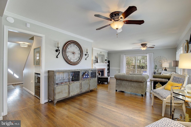 living room featuring wood finished floors, baseboards, a fireplace, ceiling fan, and crown molding