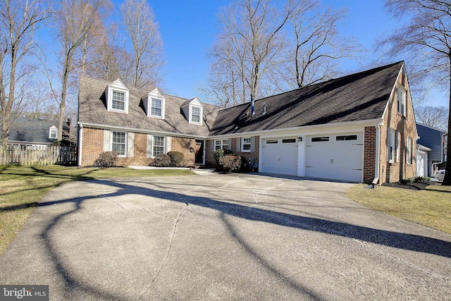 new england style home featuring fence, driveway, roof with shingles, a garage, and brick siding