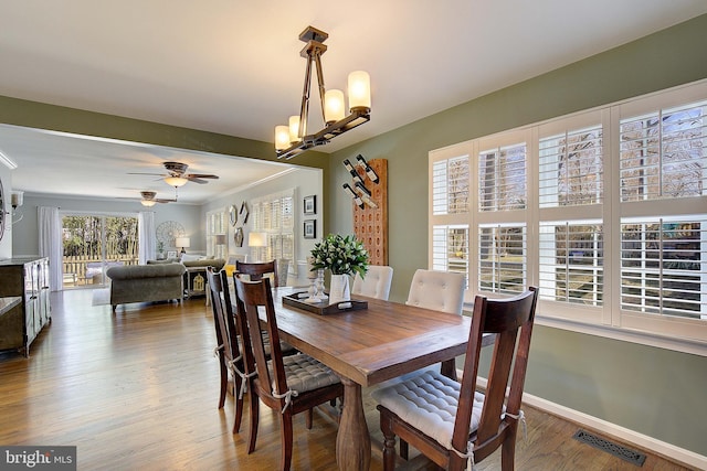 dining space featuring wood finished floors, visible vents, baseboards, crown molding, and ceiling fan with notable chandelier